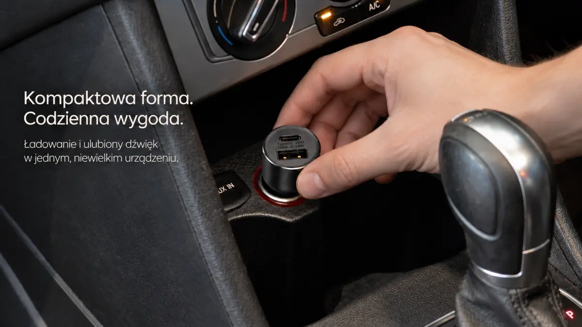 A hand placing a black FM transmitter with USB-A and USB-C ports into a car cigarette lighter socket.