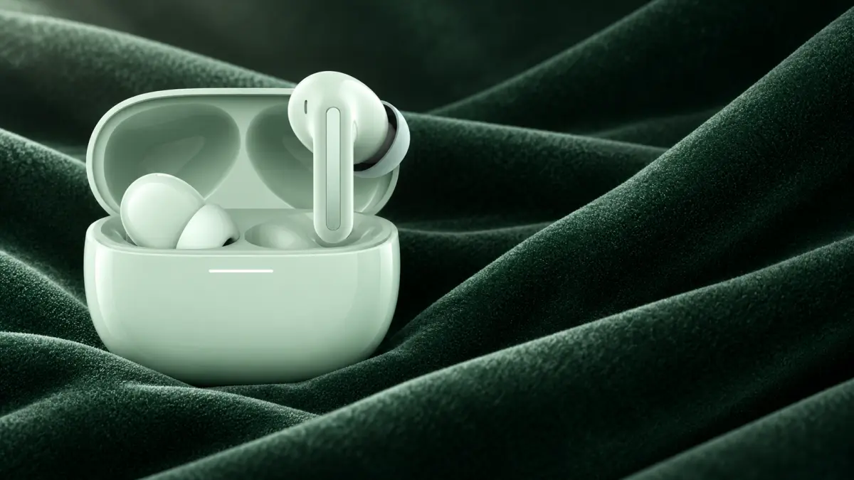 Mint wireless earbuds in an open case on wrinkled dark green fabric.