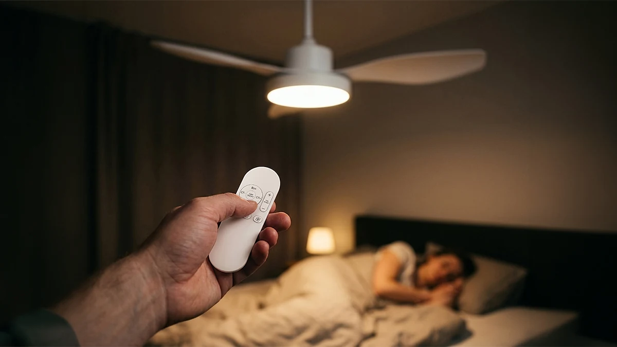 White ceiling fan with lighting, controlled by remote control, against the background of a bedroom.